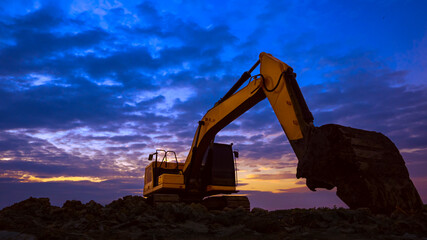 Silhouette low angle view of excavator working to land leveling in construction site against sunset...