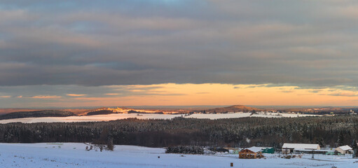 winter snowy landscape, with fields, forests and hills, at sunset