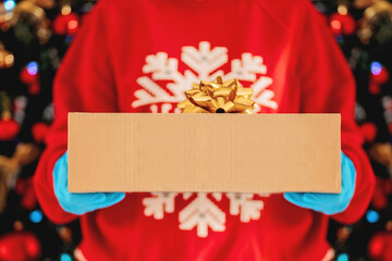  Delivery gift. Delivery man holding cardboard boxes in medical gloves on the background of a Christmas tree. Fast and free Delivery transport . Online shopping. sale. 