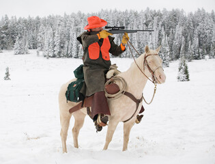adult cowboy deer hunter aiming deer rifle in snowy wilderness