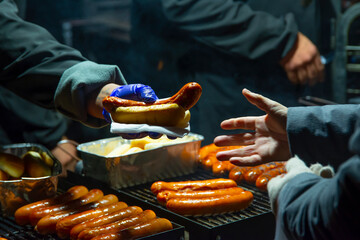 Man prepare cook hot dog on coal fire on the street during the Christmas market, selling hot dogs,...