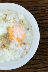 Homemade Thai Rice Soup With chicken, pork and Soft boiled egg or onsen egg in white blow on rustic wooden background. Thai style Food. Top view.