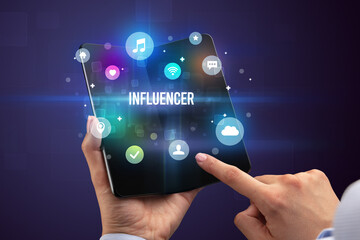 Businessman holding a foldable smartphone with INFLUENCER inscription, social media concept