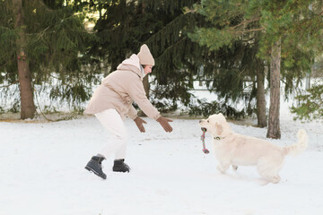 Young woman running on snow together with her dog and playing with toy outside