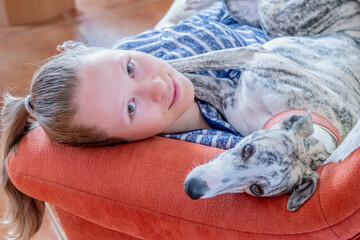 ein junges Mädchen und ihr Whippet Hund kuscheln zu Hause auf dem roten Sofa 