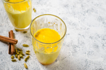 Golden milk is a traditional Indian hot drink made from milk with spices such as turmeric, cardamom, and cinnamon. Yellow milk drink in glasses on light background