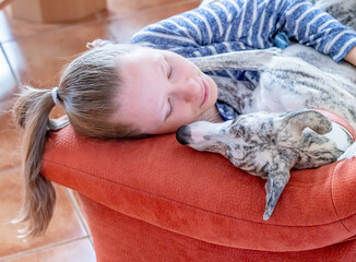 ein junges Mädchen und ihr Whippet Hund kuscheln zu Hause auf dem roten Sofa 