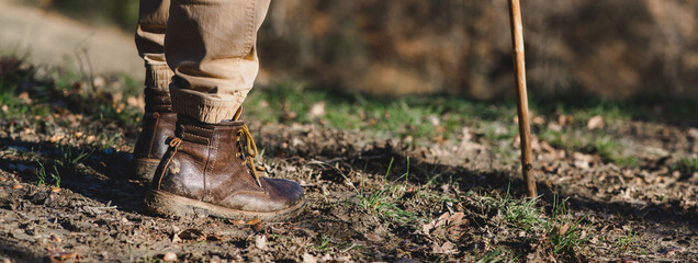 Horizontal banner close-up dirty boots of hiker man walking in a muddy path. Unrecognizable person...