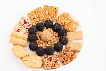 Makar Sankranti Lohri Festival Celebration - Assorted Til Gul Sweet Desserts Gud Ki Rose Chikki Black Kala Laddu Gur Rewari Tilkut Rolled Gajak Patti Gazak Papadi. White Background With Space For Text