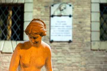 Statua, scultura imitazione di statua di età romana in ambientazione di città storica con edifici caratteristici. Fotografia notturna con luce artificiale.