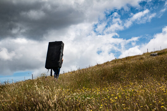 climber carrying a crash pad over a grassy hill