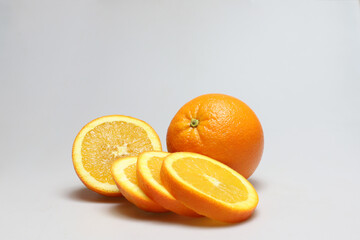 One whole and one half freestanding orange fruits next to each other with orange slices in front on a white background