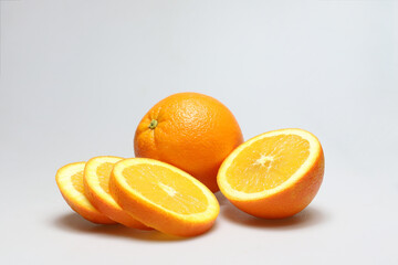 One whole freestanding orange fruit and one half of orange with orange slices in front on a white...