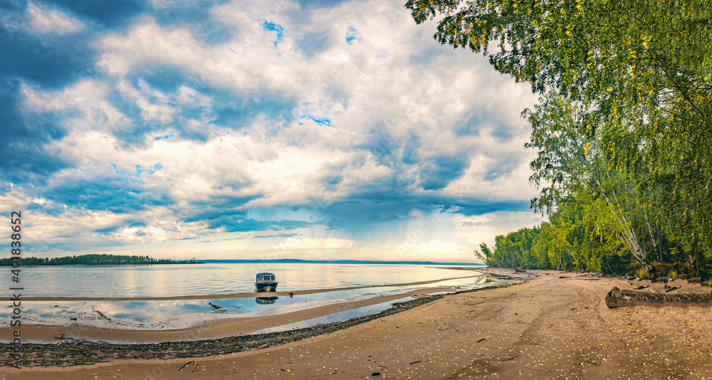 Wall mural dramatic autumn landscape with clouds, sandy river bank with fallen leaves. boat at the shore.