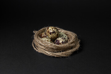 Quail eggs on a black background. Healthy food. Quail eggs lie in a nest made of jute thread