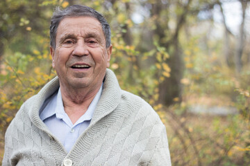 Portrait of happy senior man smiling, in the public park, outdoors. Old man relaxing outdoors and looking at camera. Portrait of elderly man enjoying retirement