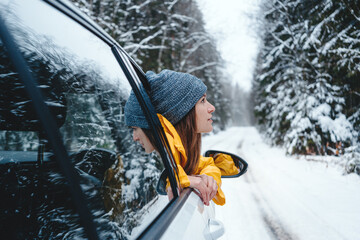 Handsome woman traveler looking away winter forest from windows of car. Girl wearing yellow jacket...
