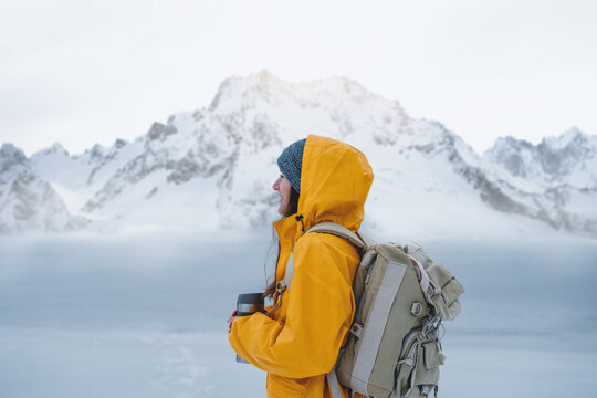 Alone brave woman traveler with backpack looking away to winter mountains. Female explorer wearing rucksack among winter landscape travel at holidays journey