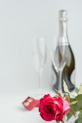 Blurred image of glasses and a bottle of champagne, a box with a ring, in the foreground a rose.