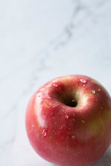Manzana roja aislada con gotas de agua sobre fondo vertical de marmol blanco