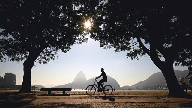 People Cycling Under Trees in Front of the Botafogo Beach in the Morning With Sugarloaf Mountain in the Horizon, Rio de Janeiro, Brazil
