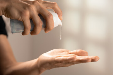 Hands of young man pressing dispenser of cosmetic gel while dropping it on palm