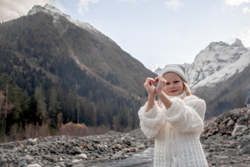 Portrait of preteen blond girl dressed in knitted warm hat,  white sweater , standing by the river....