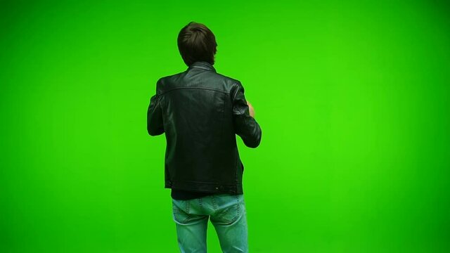 Man in jacket resting and dancing over green screen background at studio. Back view. Slow motion