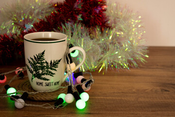 coffee mug with 'home sweet home' on it close-up and christmas decorations on wooden table background with colorful lights. Stay home new year. Top view and space for text