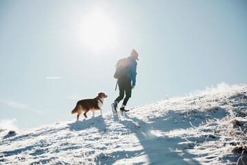 Wandernde Frau mit Hund im Schnee am Bergkamm
