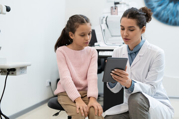 Young female ophthalmologist showing schoolgirl result of check-up of eyesight