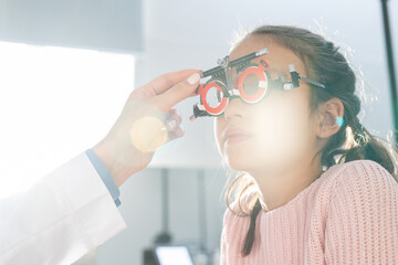 Elementary schoolgirl having check-up of eyesight with optometrist trial frame