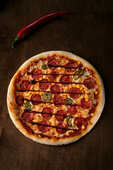 Spicy pepperoni pizza with corn and jalapeno pepper on a dark wooden background. Top view of a cooked barbecue pizza. Flat lay. Banner