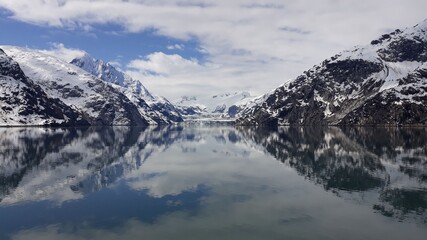 Beautiful Alaskan wilderness. Snow covered mountain tops with a reflection in the sea. View from the cruise ship in Glacier Ba. Beginning of the tourist season in Alaska 