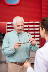 Obraz premium Senior man looking at his eyeglasses while consulting with young ophthalmologist