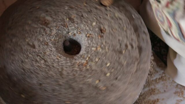 A closeup of girl filling the wheat seeds into the vintage stone grain mill grinder