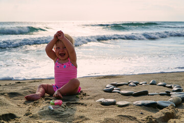 Fototapeta na wymiar Happy baby in the sand plays. Cheerful little kid playing on the beach on a sunny day. High quality photo