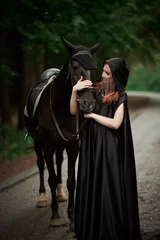 Foto op Canvas Young woman in hat and black cloak with a horse in the forest © Владимир Николаев