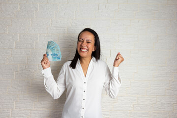Dark tone skin older woman holding brazilian banknotes currency. Economy, salary, credit, payment,...