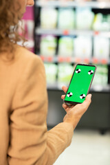 Hand of young female shopaholic holding smartphone with green screen