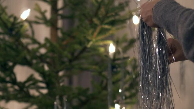 Woman preparing for X-mas celebrations, hanging silver decorations in Christmas tree on the Night Before Christmas