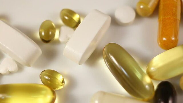 White, yellow, brown, transparent, black, oval and oblong tablets, pills, capsules are brushed out of the frame. Close-up, real time, on a white background