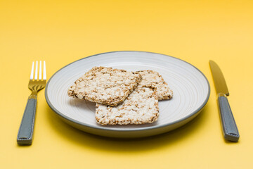 Healthy eating. Crispbread made from oats, wheat, flax and sesame seeds on a plate and cutlery on a yellow background