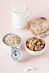 Good sleep. Foods for good sleep - milk, walnuts, crispbread, oatmeal and alarm clock on pink background. Vertical view