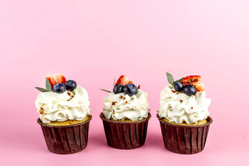 Delicious cupcakes with cream and fresh berries isolated on pink background. Copy space.