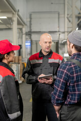 Confident bald mature foreman with tablet having discussion with subordinates