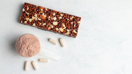 Scoop of whey or soy protein isolate, chocolate protein bar, white capsules of amino acids and creatine, bodybuilding food supplements on white background, top view, flat lay
