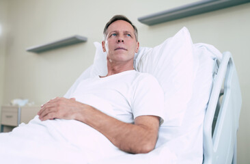 Thoughtful mature patient man is lying on the clinic bed in a hospital ward and looking away