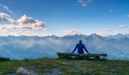 Fototapeta premium person sitting on a bench while admiring the view with mountains