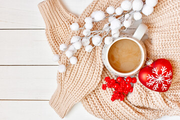 Winter background with cup of cappuccino, knitted sweater, fluffy branch, red berries and red heart.